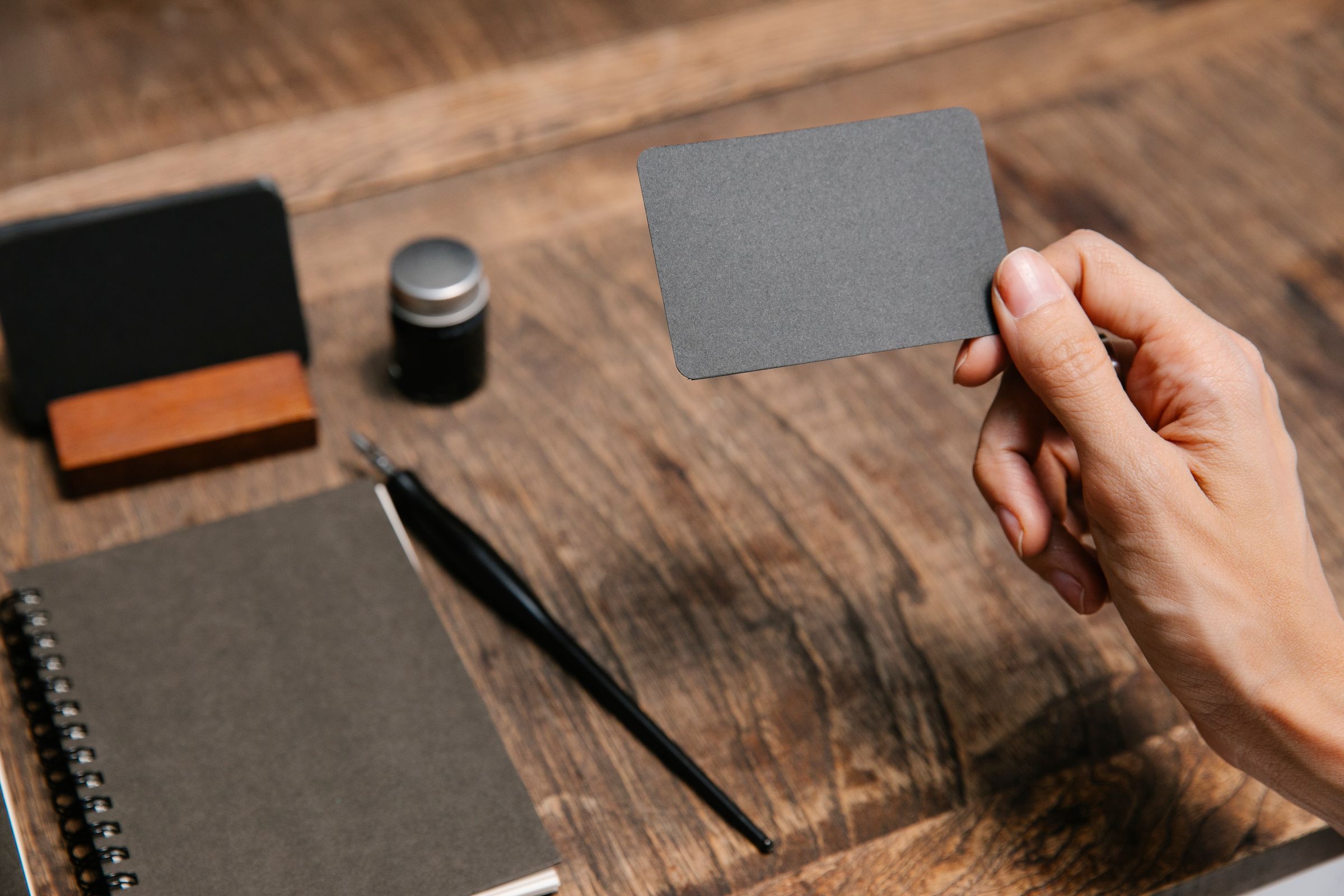 Hand holding a blank business card over a desk with a notebook and pen