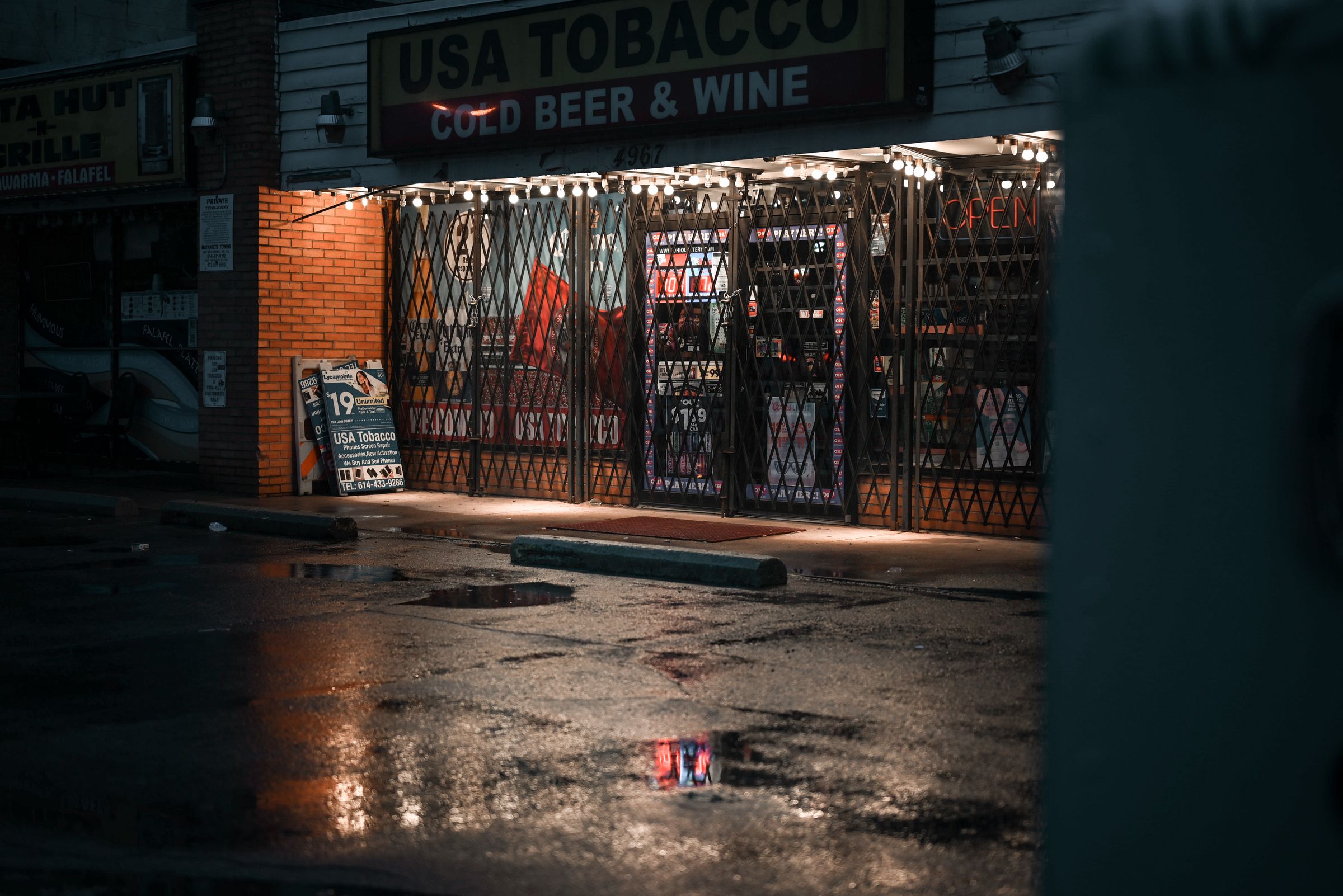 Tobacco shop storefront lit up at night on a wet street
