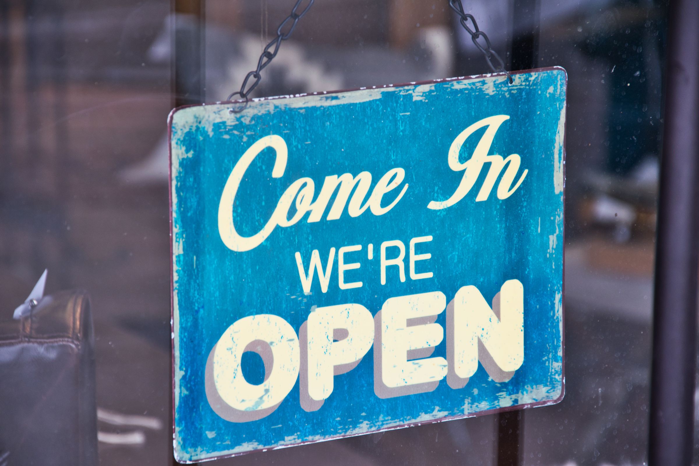 Vintage "Come in, we're open" sign hanging in a shop window
